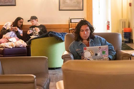 Students sit in the Carriage House, working on laptops and talking together